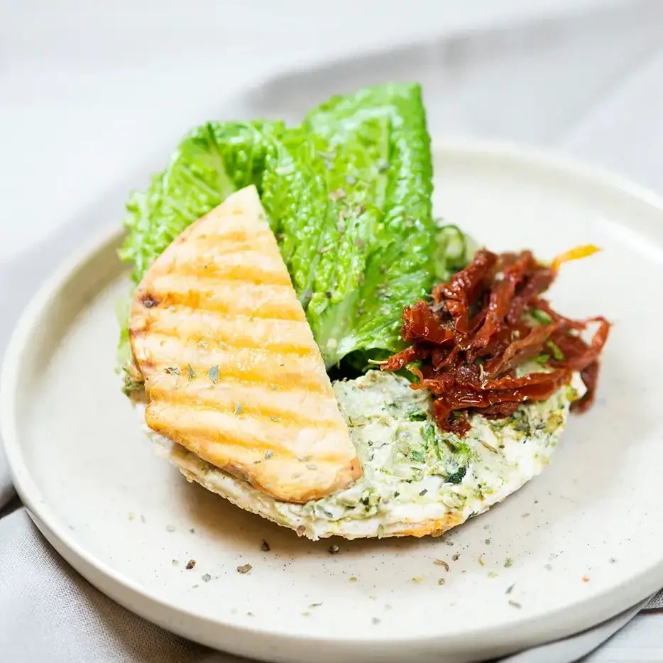 halber Bagel mit mit Basilikumpesto, Frischkäse, Ziegenkäse, getrocknete Tomaten und Salat.