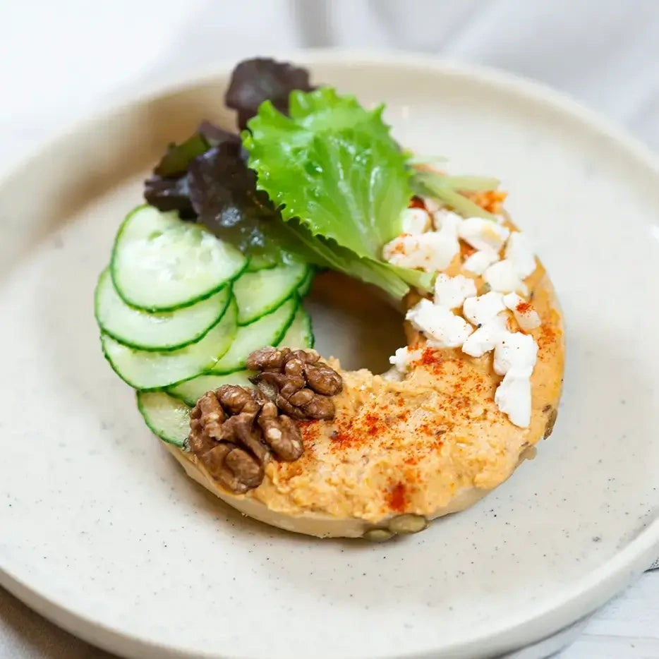 halber Bagel mit Paprika-Feta-Creme, Gurke, Walnüsse und Honig.