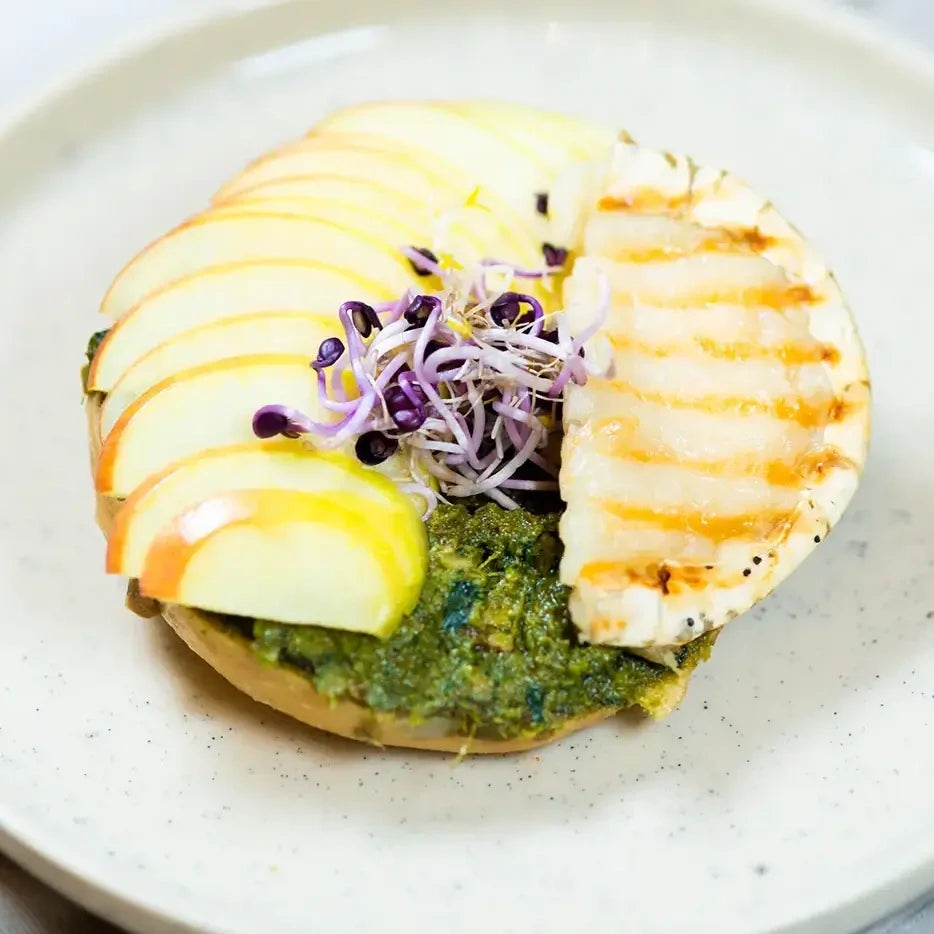 halber Bagel mit Basilikumpesto, Ziegenkäse, Apfel und gerösteter Sesam.