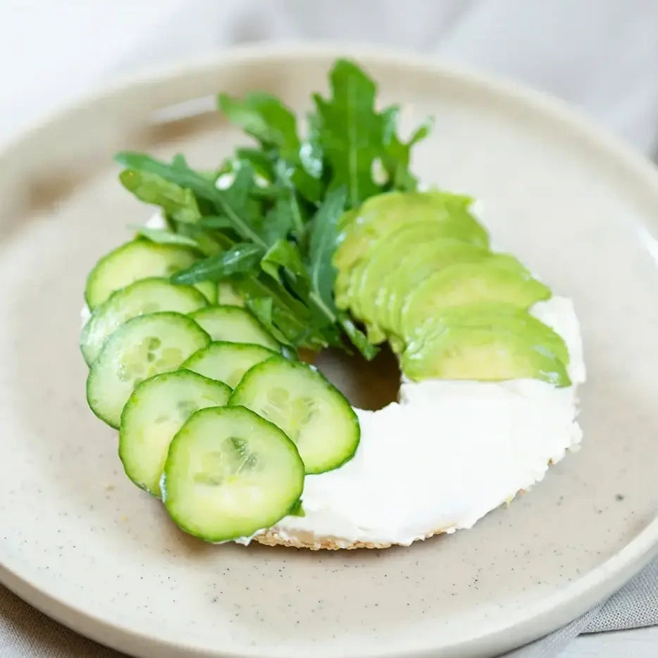 halber Bagel mit  Frischkäse, Avocado, Gurke, Salat und geröstetem Sesam.