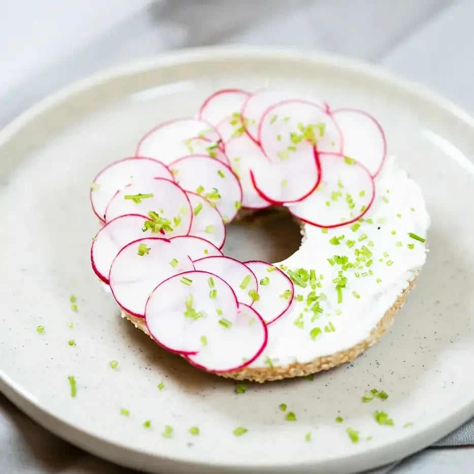 halber Bagel mit Frischkäse, Radieschen und Schnittlauch.