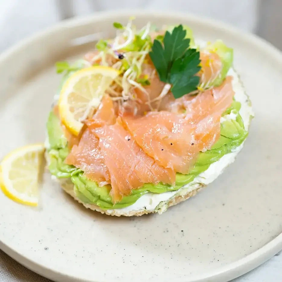 halber Bagel mit Frischkäse, Lachs, Avocado und Sprossen.