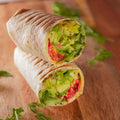 halbes Wrap mit mit Basilikumpesto, Salat, Avocado, Gurke, Tomate und Frühlingszwiebeln.
