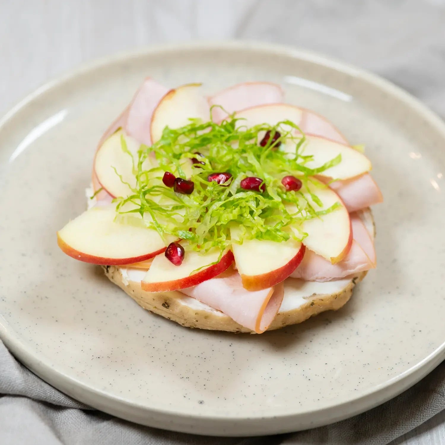halber Bagel mit Frischkäse, Hähnchenbrust, grünem Apfel und Rucola.