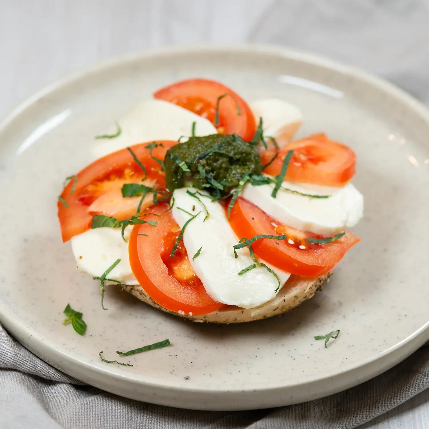 halber Bagel mit Basilikumpesto, Tomate, Büffelmozzarella und Rucola.