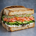 Sandwich mit Frischkäse, Avocado, Lachs, Sprossen und Salat.